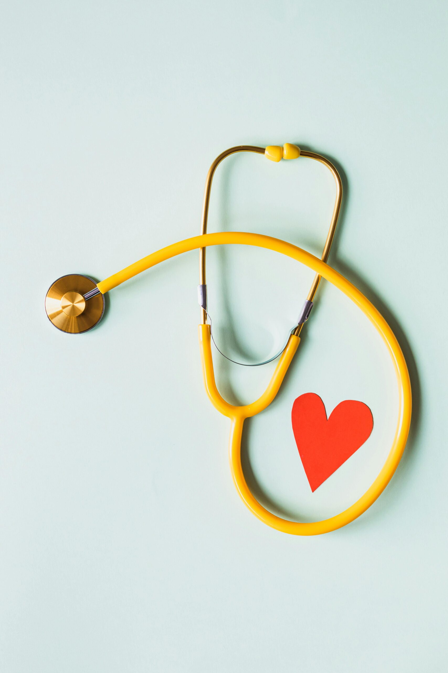 About Yellow stethoscope arranged with a red heart cutout on a light green background, symbolizing heart health.